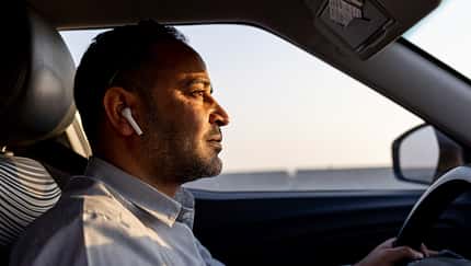 Mann fährt mit Kopfhörern Auto.