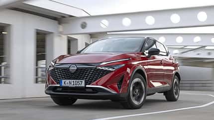 Nissan Qashqai e-Power 156 in Rot, fahrend in urbaner Umgebung, Front- und Seitenansicht.