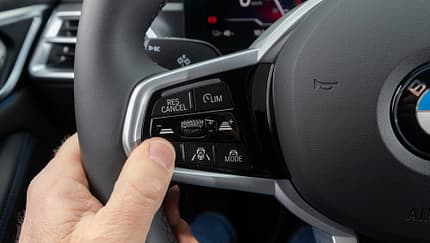 Detailaufnahme des Multifunktionslenkrads eines BMW i4 xDrive40 Gran Coupe, Fokus auf Bedientasten für Assistenzsysteme.