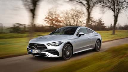 Mercedes CLE 300e Coupe fährt auf einer Landstraße, silberfarben, Coupé-Design, herbstliche Umgebung.