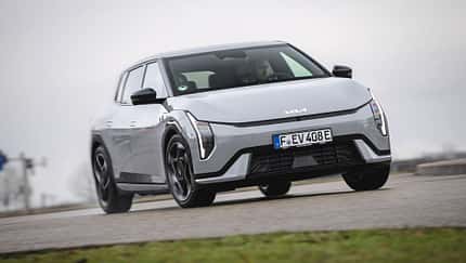 Kia EV4 GTline, Elektroauto, Kia, Stadtfahrzeug, Crossover, 2025, E-Mobilität, Frontansicht, Straßenfahrzeug, Automobil Kia EV4 GTline auf einer Straße, Fahrzeug frontal leicht von unten fotografiert, graues Wetter, urbaner Kontext.