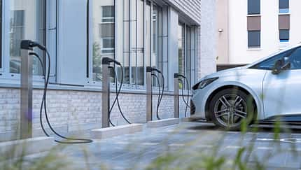 Mehrere MAHLE charge BIG und Smallbox Ladesäulen für Elektrofahrzeuge vor einem modernen Gebäude, ein Elektroauto ist angeschlossen.