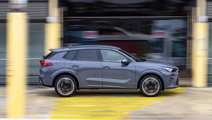 Seitenansicht eines fahrenden Cupra Terramar VZ 2.0 TSI 195 kW SUV in Grau vor urbanem Hintergrund.