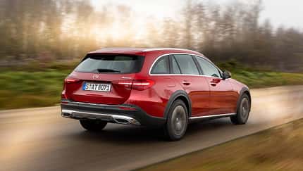 Mercedes C220d 4matic All-Terrain in Rot fährt auf einer Landstraße, fotografiert von schräg hinten, unscharfer Hintergrund.