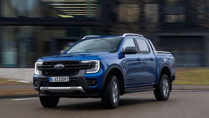 Ford Ranger PHEV 2.3L EcoBoost fährt auf einer Straße, blauer Pickup, Front- und Seitenansicht, Tageslicht.