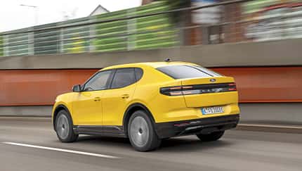 Gelber Ford Capri Extended Range 79kWh fährt auf einer Straße, fotografiert von hinten in Bewegung.