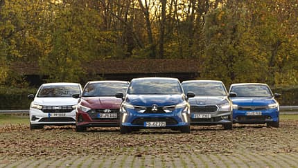 Fünf Kleinwagen-Modelle (Mitsubishi Colt, Dacia Sandero, Opel Corsa, Skoda Fabia, Hyundai i20) nebeneinander auf einem Parkplatz in herbstlicher Umgebung, frontal fotografiert.