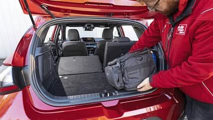 Hyundai i20 T-GDI, Kofferraum, Kompaktwagen, umgeklappte Rückbank, Laderaum, Gepäckraum, Auto, Beladung, Innenraum, Fünftürer Hyundai i20 T-GDI Kofferraum mit umgeklappter Rückbank, Person lädt Tasche ein.