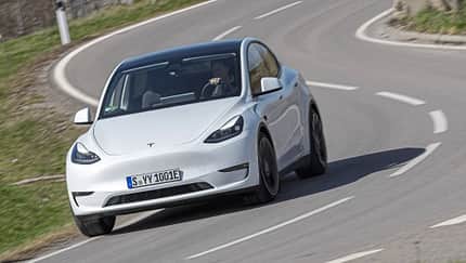 Tesla Model Y, Dauertest, Elektro-SUV, Tesla, Elektroauto, Langzeittest, Straßenfahrt, Fahrbericht, Automobil, E-Mobilität Tesla Model Y in weiß auf einer kurvigen Landstraße während eines Dauertests, frontal fotografiert.