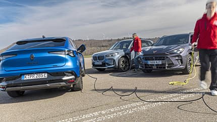 Renault Rafale Hyper Hybrid E-Tech, BMW X1 xDrive 30e, Cupra Terramar VZ e-Hybrid, Plug-in-Hybrid, SUV, Ladeszene, Elektromobilität, Vergleichstest, Ladestation, Gruppenaufnahme Drei Plug-in-Hybrid-SUVs (Renault Rafale Hyper Hybrid E-Tech, BMW X1 xDrive 30e, Cupra Terramar VZ e-Hybrid) werden auf einem Parkplatz geladen. Zwei Personen in roten Jacken hantieren mit Ladekabeln.