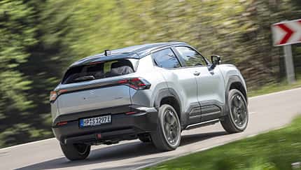 Suzuki e-Vitara eAxle, silberner Elektro-SUV, fährt auf Landstraße, Rückansicht, Frühjahr 2024.