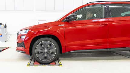 Skoda Karoq, SUV, Fahrzeugtest, Rollenprüfstand, Automobil, Werkstatt, Frontantrieb, Fahrzeugprüfung, 2024, Crossover Rotes Skoda Karoq SUV, Seitenansicht, auf Rollenprüfstand in heller Werkstattumgebung, Fahrer am Steuer.