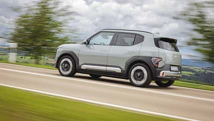 Der Dateiname nennt das Modell "Kia EV2 RG26". Das Bild zeigt einen Kia EV2 RG26 als SUV in Seitenansicht auf einer Landstraße in Bewegung. Die Aufnahme ist dynamisch, mit unscharfem Hintergrund und klar erkennbarem Fahrzeug.