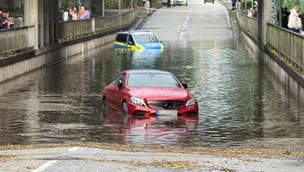 07/2026, Wasserdurchfahrt Panne Polizei Ein Polizeiauto und ein roter Mercedes stehen hüfthoch in einer überschwemmten Straßensenke