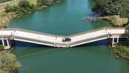 07/2026, Defekte Brücke Griechenland Eine Straßenbrücke, die in der Mitte zusammengebrochen ist, ist aus der Vogelperspektive zu sehen. Die Fahrbahn liegt knapp über einem Fluss und wird von einem Pickup befahren.