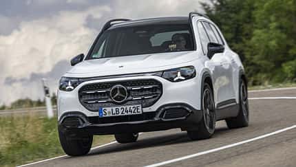 Mercedes GLB 250+ auf Landstraße, Frontansicht, weißes SUV, dynamische Kurvenfahrt, Tageslicht.