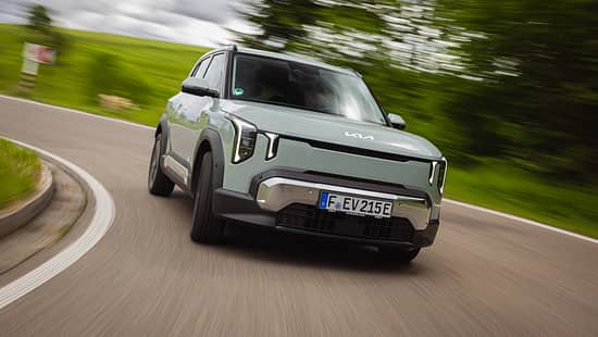 Kia EV2 auf Landstraße in Kurvenfahrt, Frontalansicht, dynamische Bewegungsunschärfe im Hintergrund.