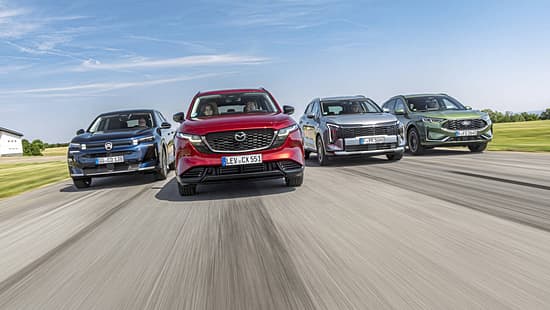 Vier aktuelle SUV-Modelle (Citroën C5 Aircross Hybrid, Mazda CX-5, Kia Sportage, Ford Kuga) fahren nebeneinander auf einer Landstraße. Die Fahrzeuge sind frontal und dynamisch im Verband aufgenommen, alle Modelle sind klar erkennbar.