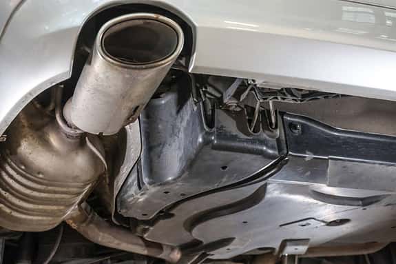 Wir bleiben auf der Hebebühne und bewegen uns ans Kombiheck. V-Motoren haben eine Doppelflutige Abgasanlage, doch auch bei Vierzylinder sitzt der Endtopf fahrerseitig. Warum? Der Auspuff an sich kennt keine Rostprobleme. Aber gleich beim Endrohr sitzt bei den T-Modellen, bzw. Autos mit Airmatic der Luftkompressor für die Luftfederung (im T-Modell ist die Hinterachse immer luftgefedert). Während das Fahrwerk selbst relativ unkritisch ist, kommt es unter der hier gezeigten Kunststoffabdeckung durch eingeschleuderten Schmutz und Feuchtigkeit ab und zu Schäden an den Elektrokabeln. So lässt sich ein im Kombiinstrument noch teuer aussehender Fahrwerksfehler mit fünf Minuten Arbeiten am Lötkolben reparieren.