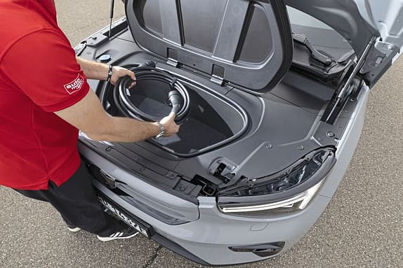 Eine Person legt ein Ladekabel in den vorderen Kofferraum (Frunk) eines Elektroautos.