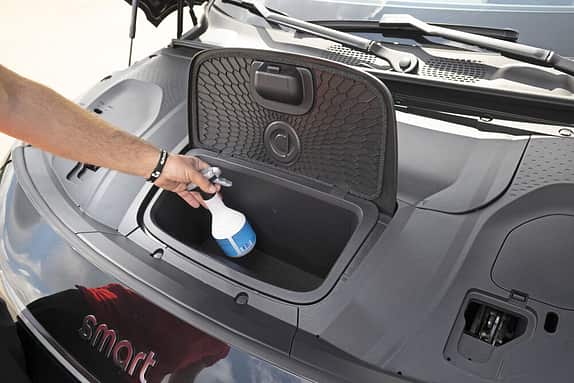 Eine Person legt einen Gegenstand in ein Staufach im vorderen Bereich eines Smart-Autos.
