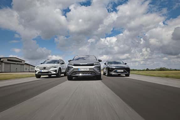 Drei moderne SUVs fahren nebeneinander auf einer Straße, fotografiert aus der Froschperspektive. Der Himmel ist bewölkt, die Szene wirkt dynamisch.