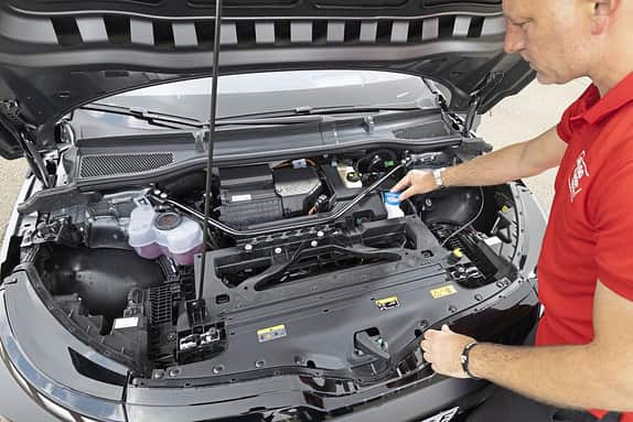 Ein Mann prüft oder befüllt Flüssigkeiten im Motorraum eines Autos mit geöffneter Motorhaube.
