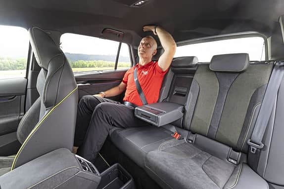 Ein Mann sitzt auf der Rückbank eines Autos und prüft den Abstand zum Fahrzeugdach mit seiner Hand.