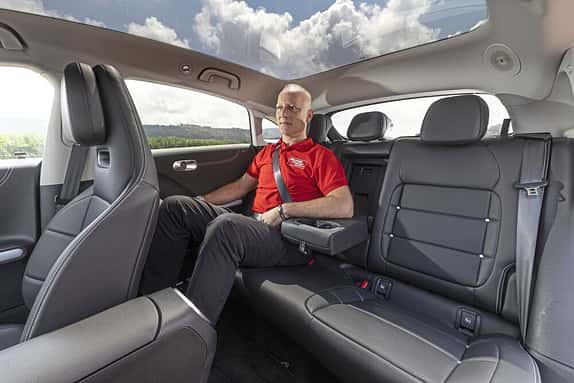 Ein Mann sitzt auf der Rückbank eines Autos mit Panoramadach. Die Aufnahme zeigt den Innenraum des Fahrzeugs.