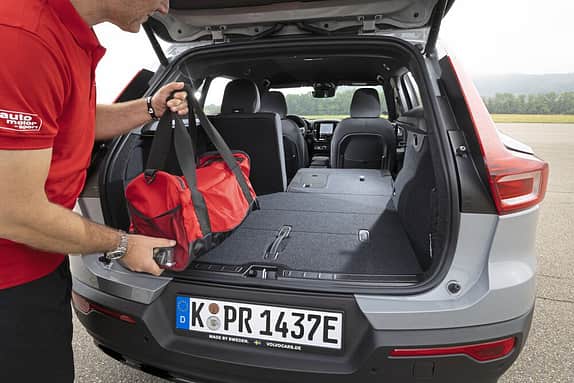 Eine Person lädt eine rote Sporttasche in den Kofferraum eines Autos mit umgeklappten Rücksitzen.
