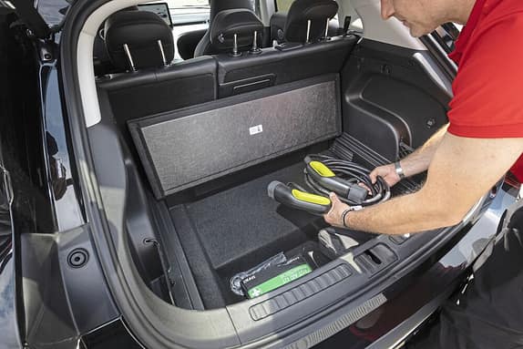 Ein Mann legt ein Ladekabel in das Kofferraumfach eines Autos. Im Hintergrund sind die Rücksitze und ein Bildschirm sichtbar.