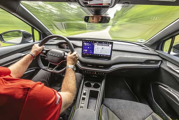 Innenraum eines fahrenden Autos, Blick aus der Perspektive des Fahrers auf das Lenkrad, das Armaturenbrett und das zentrale Display. Ein Mann steuert das Fahrzeug.