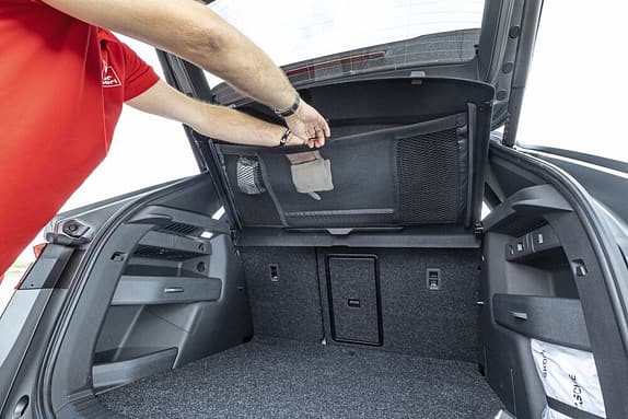 Ein Mensch öffnet das Gepäckraumfach eines Autos und hebt das Gepäckraumrollo mit integriertem Netz an.