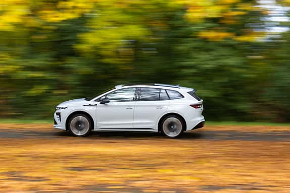 Weißer Skoda Enyaq RS 79 kWh fährt auf herbstlicher Straße, Seitenansicht, unscharfer Hintergrund durch Mitzieheffekt.
