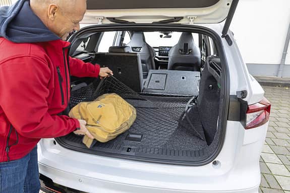 Kofferraum des Skoda Enyaq RS 79 kWh mit umgeklappter Rückbank, ein Mann verstaut eine Tasche unter einem Gepäcknetz.
