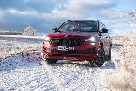 Roter Skoda Karoq 2.0 TDI 4x4 auf verschneiter Landstraße in winterlicher Landschaft, Frontalansicht.