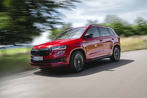 Skoda Karoq 4x4 in Rot fährt auf einer Landstraße, dynamische Außenaufnahme, Fahrzeug in Bewegung.
