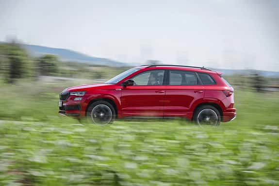 Rotes Skoda Karoq 4x4 SUV fährt seitlich durch grüne Landschaft, Bewegungsunschärfe im Hintergrund.
