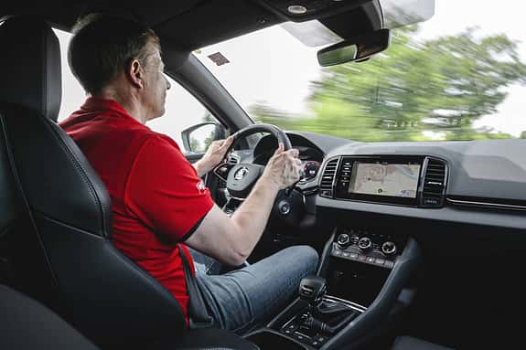 Innenaufnahme eines fahrenden Skoda Karoq 4x4 mit Fahrer, Blick auf Cockpit, Lenkrad und Infotainmentsystem.