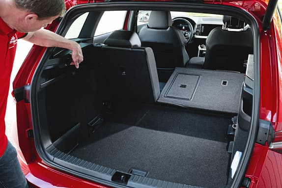 Der Kofferraum eines Skoda Karoq 4x4 mit umgeklappter Rückbank, ein Mann zeigt auf eine Funktion im Laderaum.