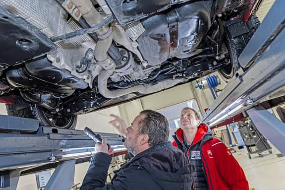 Zwei Personen inspizieren den Unterboden eines Skoda Karoq auf einer Hebebühne in einer Werkstatt.