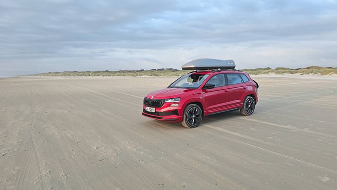 Skoda Karoq 2.0 TDI Sportline 4x4 (Modelljahr 2025) in Rot mit Dachbox auf Sandstrand, Aufnahme aus dem Dauertest.