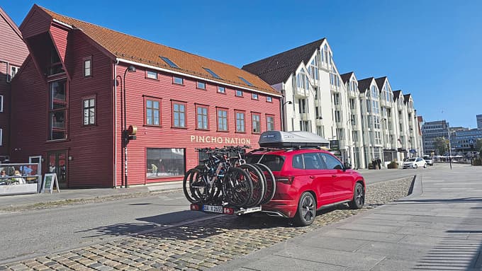 Skoda Karoq 2.0 TDI Sportline 4x4 (Modelljahr 2025) mit Fahrradträger und Dachbox vor städtischer Kulisse, aufgenommen im Rahmen eines Dauertests.