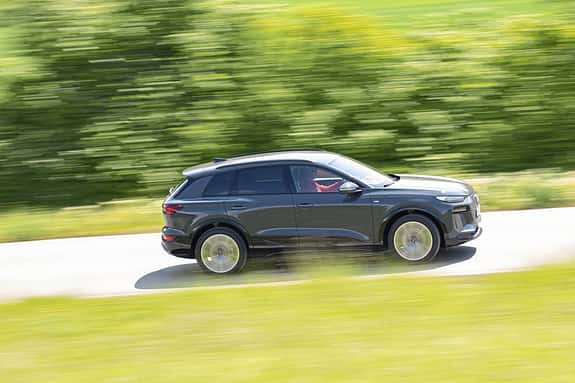 Audi Q6 SUV e-tron quattro fährt auf einer Landstraße, Seitenansicht, grüne Umgebung, Bewegungseffekt.
