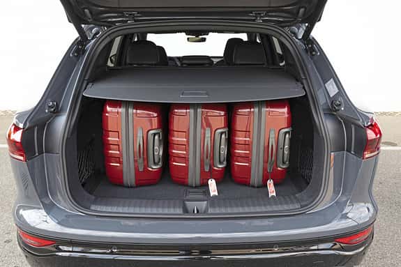 Audi Q6 SUV e-tron quattro Kofferraum mit vier roten Koffern, Heckansicht, Gepäckraum unter Abdeckung.