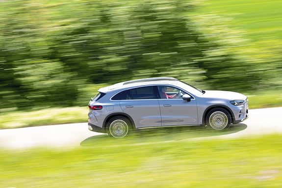 Mercedes GLC 400 4matic EQ fährt auf einer Landstraße, Seitenansicht, grüne Landschaft im Hintergrund.