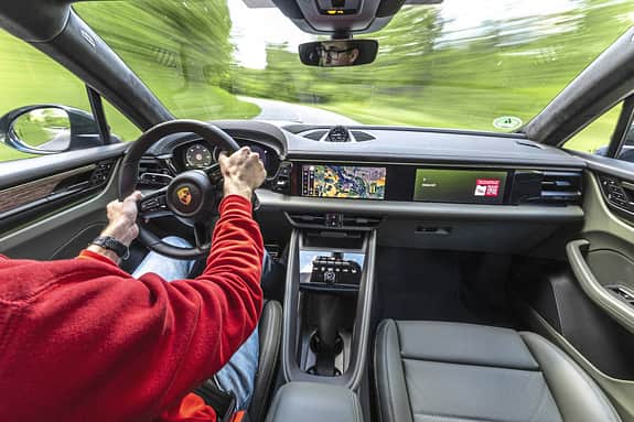 Innenraum und Cockpit eines Porsche Macan 4S während der Fahrt, Fahrer am Steuer, moderne Digitalanzeigen und Navigationssystem sichtbar.