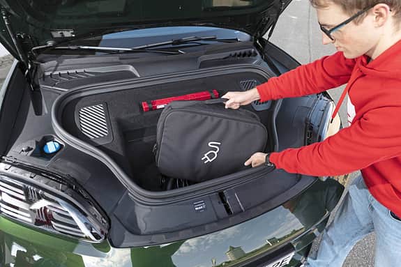 Ein Mann legt eine Tasche mit Ladesymbol in den vorderen Kofferraum eines Porsche Macan 4S.
