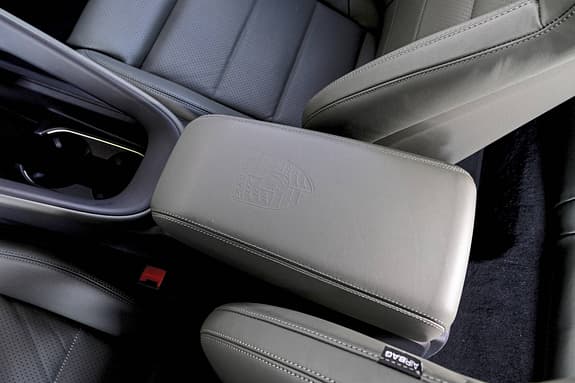 Detailaufnahme der Mittelarmlehne und Vordersitze eines Porsche Macan 4S. Das Porsche-Wappen ist auf der Lederarmlehne eingeprägt.