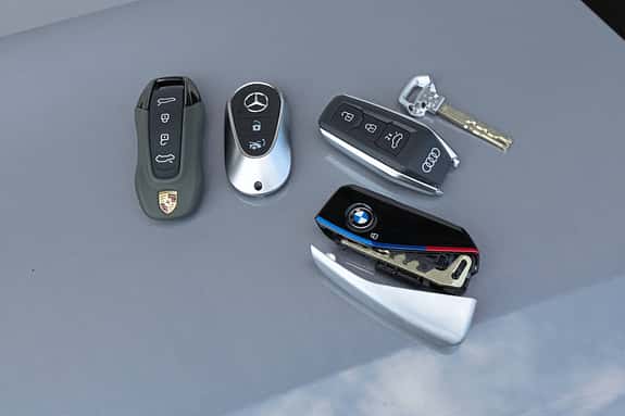 Vier Autoschlüssel von BMW, Mercedes-Benz, Audi und Porsche liegen nebeneinander auf einer glatten Oberfläche.